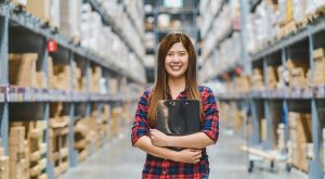 Portrait of Asian woman warehouse worker standing and holding the clipboard for checking goods stock in warehouse, business furniture and storehouse industry concept
