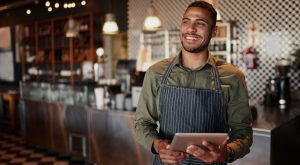 Young male owner holding digital tablet while standing in cafe