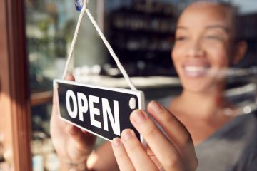 Female Owner Of Start Up Coffee Shop Or Restaurant Turning Round Open Sign On Door